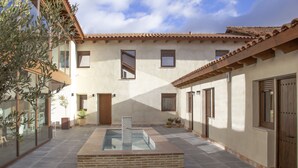 A courtyard with a pool, potted plants, and a building with a tiled roof and large windows.