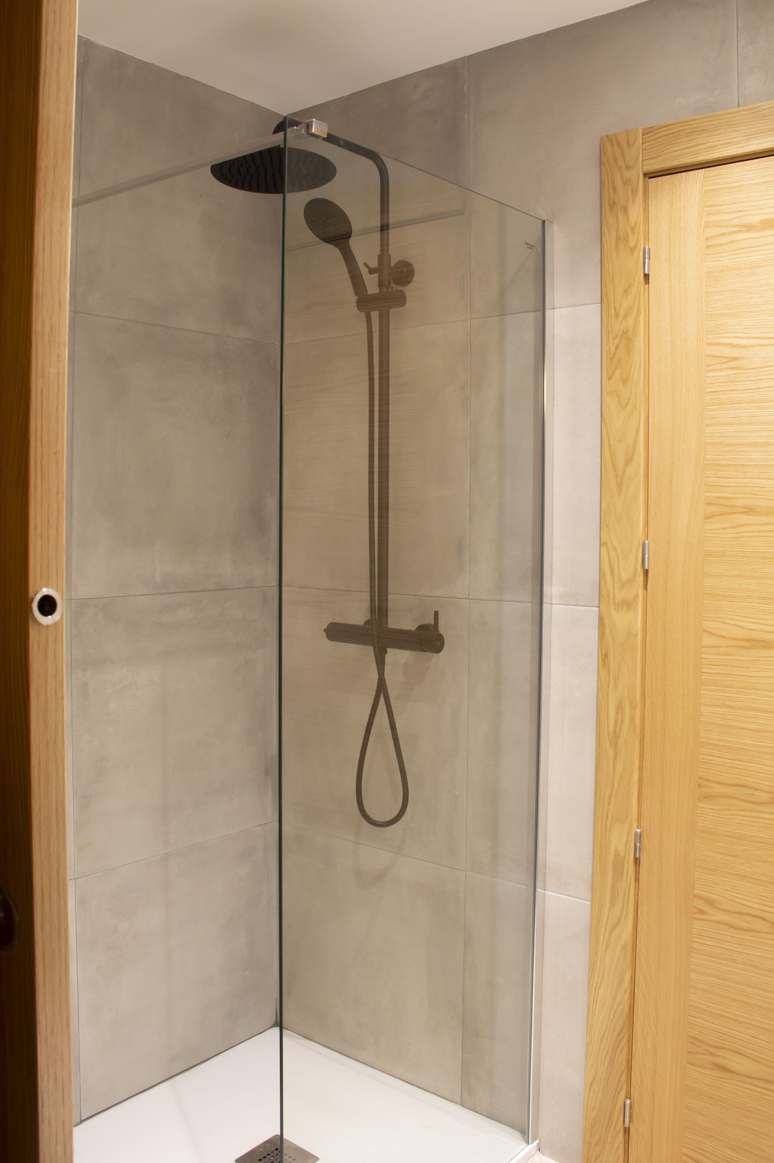 A glass-enclosed shower with a handheld showerhead and a rain shower head.