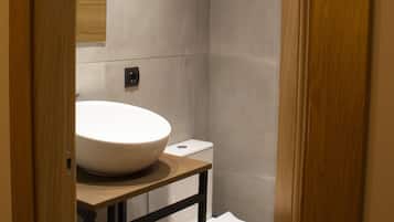 A modern bathroom with a large white sink, a toilet, and a shower area.