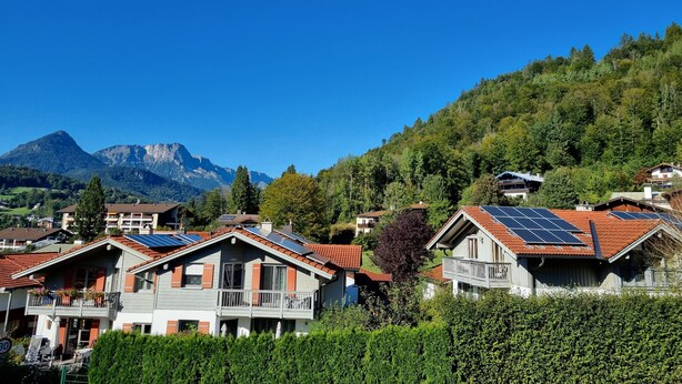 A residential area with houses featuring sloped roofs and solar panels, surrounded by lush greenery and mountains in the background. - Water lily Apartment (Berchtesgaden)