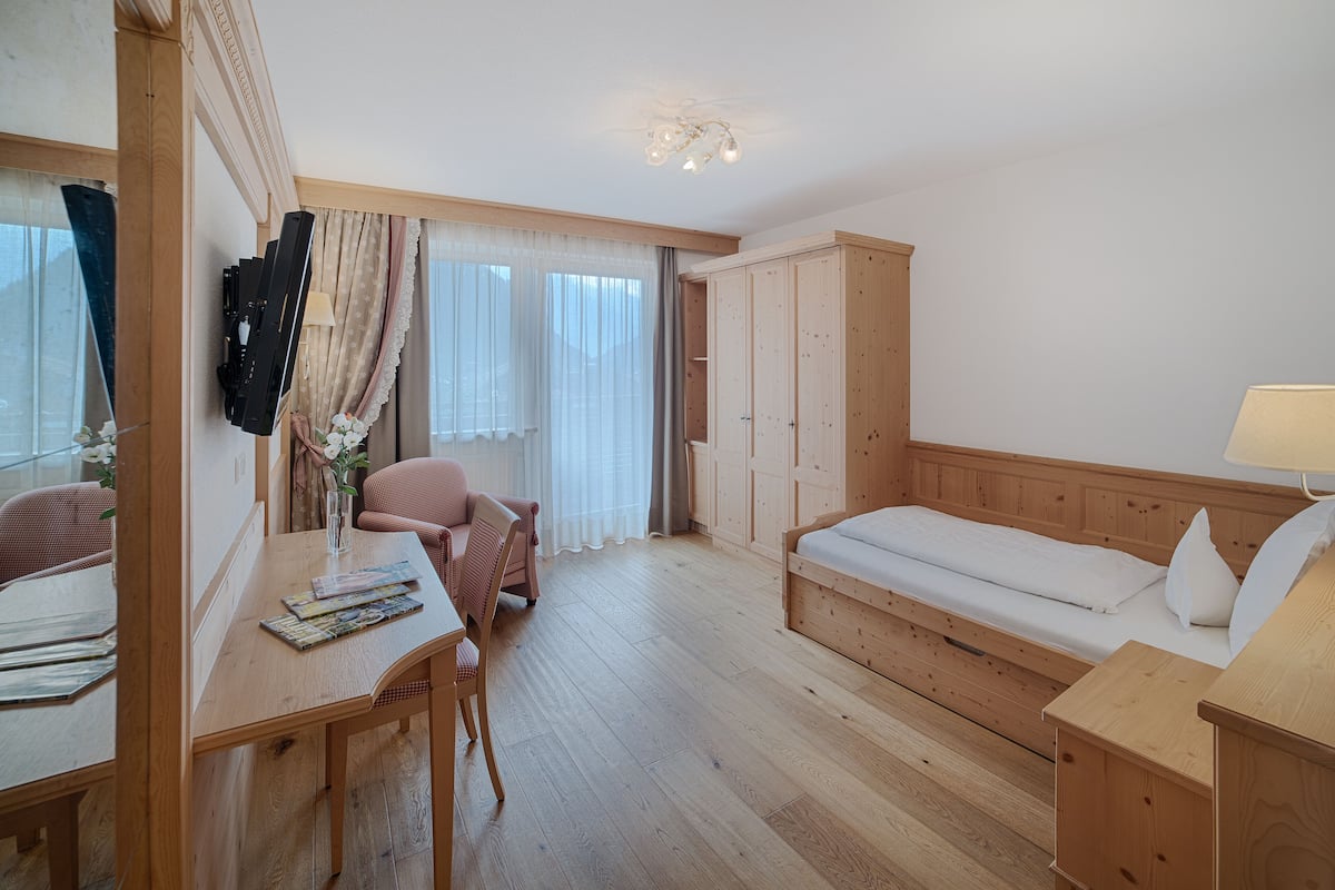 Une pièce comprenant un bureau en bois, une chaise, un lit avec une tête de lit en bois et une armoire.