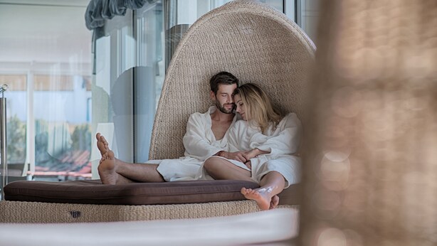 A couple in a wicker chair with a view of a cityscape. - Alpenblick Hotel (Valle Aurina)