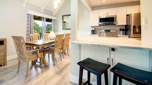 A modern kitchen with white cabinets, stainless steel appliances, and a wooden dining table with chairs.