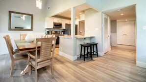 A modern kitchen with wooden cabinetry, a dining area with a wooden table and chairs, and a hallway leading to a closet.