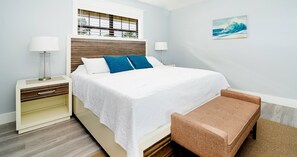 A bedroom with a bed, bedside tables, a bench, a window with blinds, and a painting on the wall.