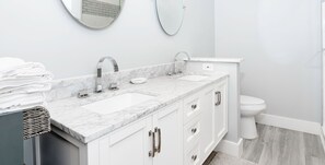 A modern bathroom with a white vanity, two sinks, and a toilet.