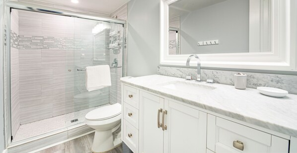 A modern bathroom with a glass-enclosed shower, a white toilet, and a marble countertop with a sink and mirror.