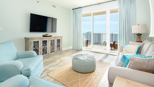 A living room with a flat-screen TV, a large window with a view of buildings, a wooden cabinet, and a sofa with a throw pillow.