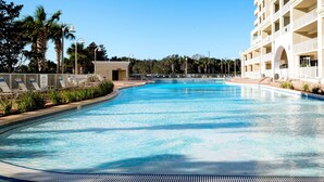 A large, clear swimming pool with lounge chairs and a small building in the background.