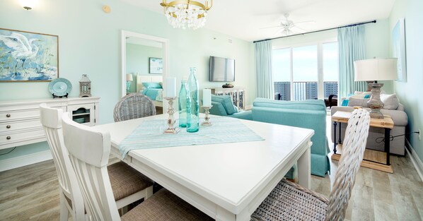 A bright living room with a white table, teal sofa, and a view of the city. - Ariel Dunes II 1503 *Beach views* 3 pools* (Destin)
