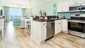 A modern kitchen with white cabinets, stainless steel appliances, and a dining area with a view.