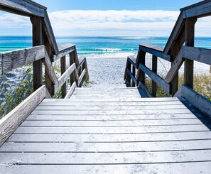 A wooden boardwalk leading to a beach with the ocean in the background.