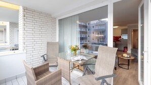 A balcony with wicker chairs, a glass table, and a vase of flowers. - Beautiful 2-room vacation apartment in city location on approx. 50 m² for up to 2 persons. (Westerland)