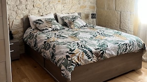 A bedroom with a stone wall, a bed with a leaf-patterned bedspread, a hanging light fixture, and a framed picture on the wall. - mas (Tarascon)
