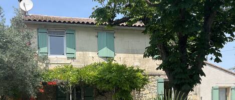 A two-story house with a tiled roof, green shutters, and a satellite dish.