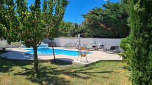A backyard with a swimming pool, lounge chairs, and a tree with fruit.