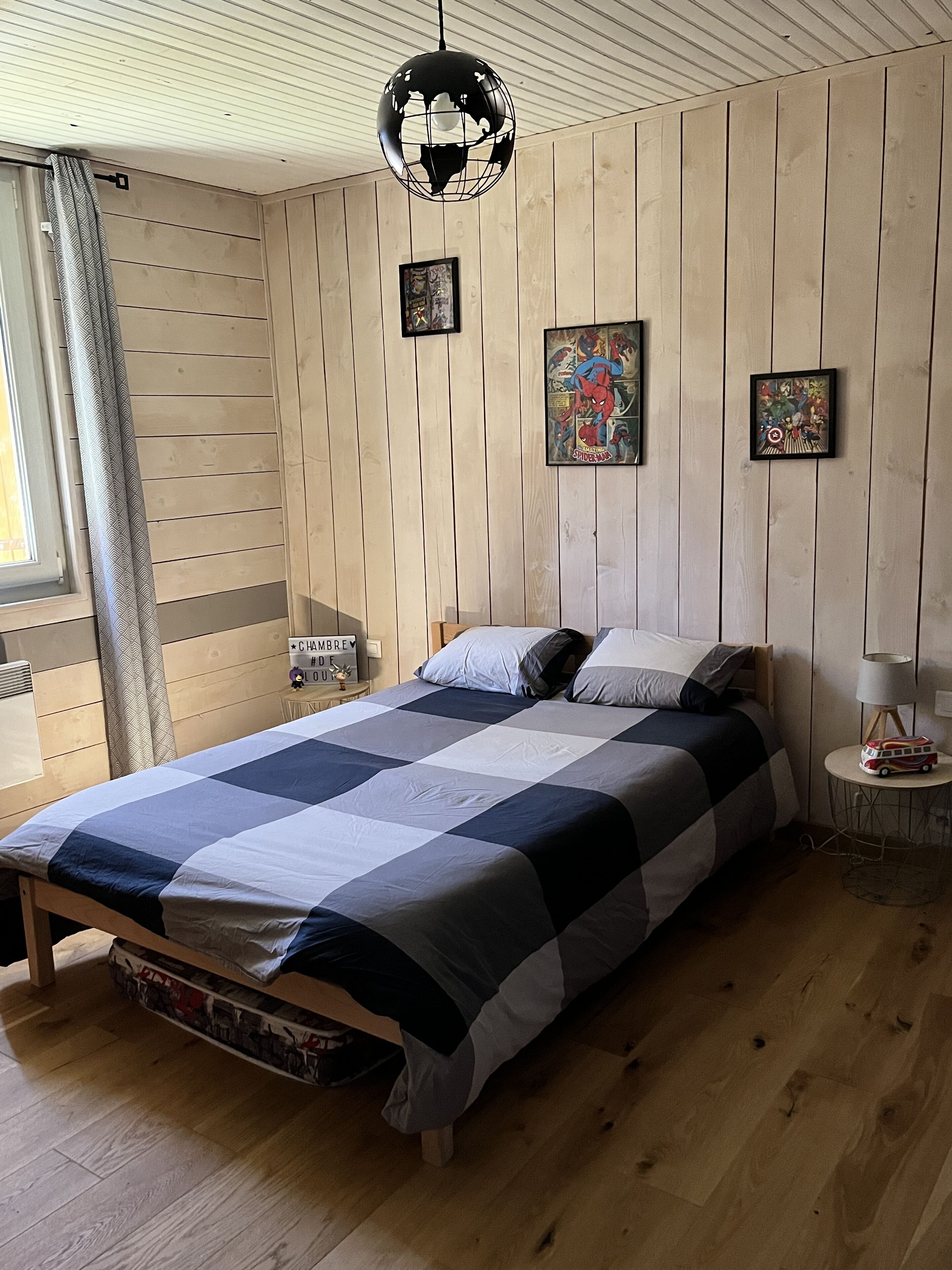 Un dormitorio con una cama de madera, una lámpara colgante tipo globo y dos carteles de cómics enmarcados en la pared.