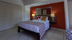 Una habitación de hotel con una cama, dos lámparas de noche, un espejo grande y una pared decorada en rojo.