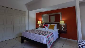 Une chambre d’hôtel avec un lit, deux lampes de chevet, un grand miroir et un mur d’accent de couleur rouge.