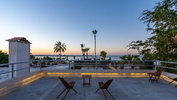 A rooftop terrace with a concrete floor, wooden lounge chairs, a small table, and a railing. Palm trees and a view of the ocean are visible in the background. - 🌿🌿 Tamarind 4 (Durango)