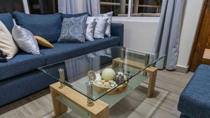 A living room with a glass coffee table, a blue sofa, and a wooden side table. - 🌿🌿 Tamarind 4 (Durango)
