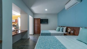 Une chambre d’hôtel avec deux lits, un téléviseur fixé au mur, un petit bureau avec une lampe et une vue sur la cuisine.