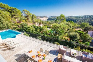 A poolside area with lounge chairs, a dining table, and a view of a forested valley.
