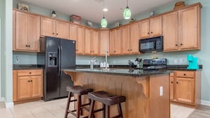 Una cocina con gabinetes de madera, un refrigerador negro, un microondas y una barra con taburetes.