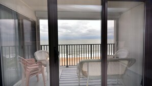 A balcony with two wicker chairs, a striped rug, and a view of the beach.