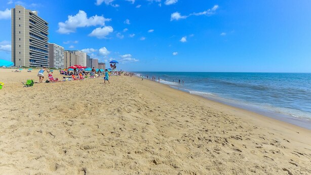 A beach with a sandy shore, umbrellas, and people.