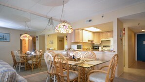 A dining area with a glass table and wicker chairs, a kitchen with wooden cabinets, and a blue door.