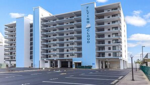A multi-story hotel named Flying Cloud with a modern architectural design, featuring balconies on each floor and a parking area in front.