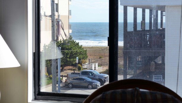 Une vue depuis une fenêtre donnant sur une plage, avec un bâtiment et des voitures garées.