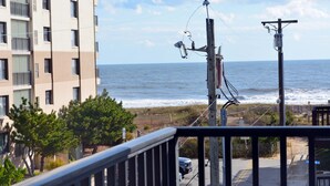 Une vue sur la côte depuis un balcon doté d’une balustrade, donnant sur l’océan et un immeuble avec de nombreuses fenêtres.