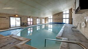 Une piscine intérieure avec des parois en verre transparent, un sol carrelé et une rambarde métallique.