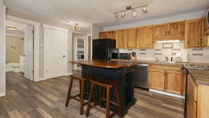 Une cuisine avec des meubles de rangement en bois, un réfrigérateur noir, un plan de travail en bois et deux tabourets de bar.