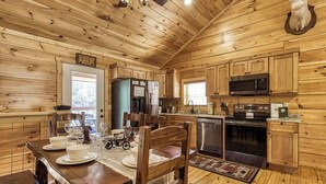 A wooden cabin interior with a dining area, kitchen, and a mounted deer head. - Sunshine Ridge, Hot Tub, Game Room, $560 FREE tickets each paid day (Sevierville)