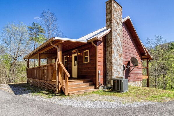 A rustic cabin with a stone chimney, wooden porch, and a gravel driveway. - Sunshine Ridge, Hot Tub, Game Room, $560 FREE tickets each paid day (Sevierville)