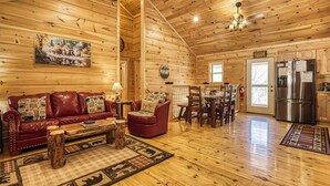 A cozy log cabin interior with a wooden ceiling, a red leather sofa, a dining table, and a kitchen area with a refrigerator. - Sunshine Ridge, Hot Tub, Game Room, $560 FREE tickets each paid day (Sevierville)