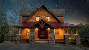 Ein Holzhaus mit rotem Dach, Steinpfeilern und einer Veranda mit einer Bank.