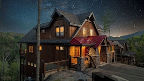 A large wooden cabin with multiple windows, a stone fireplace, and a red roof.
