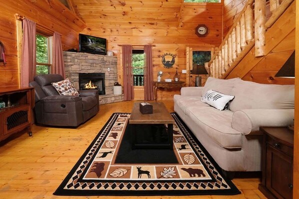 Un intérieur de chalet chaleureux avec une cheminée en pierre, un canapé en cuir et un tapis à motifs.