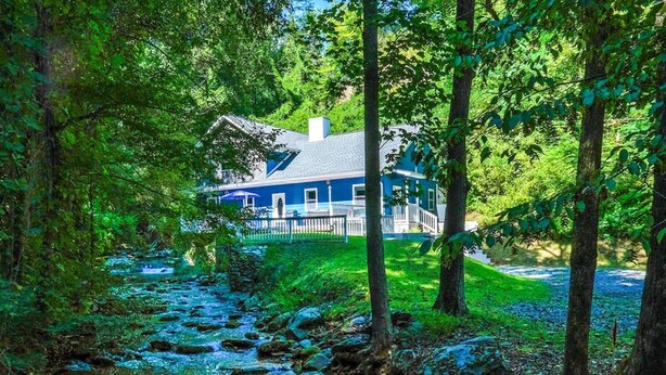 Una casa rodeada de un bosque frondoso con un arroyo que atraviesa la propiedad.
