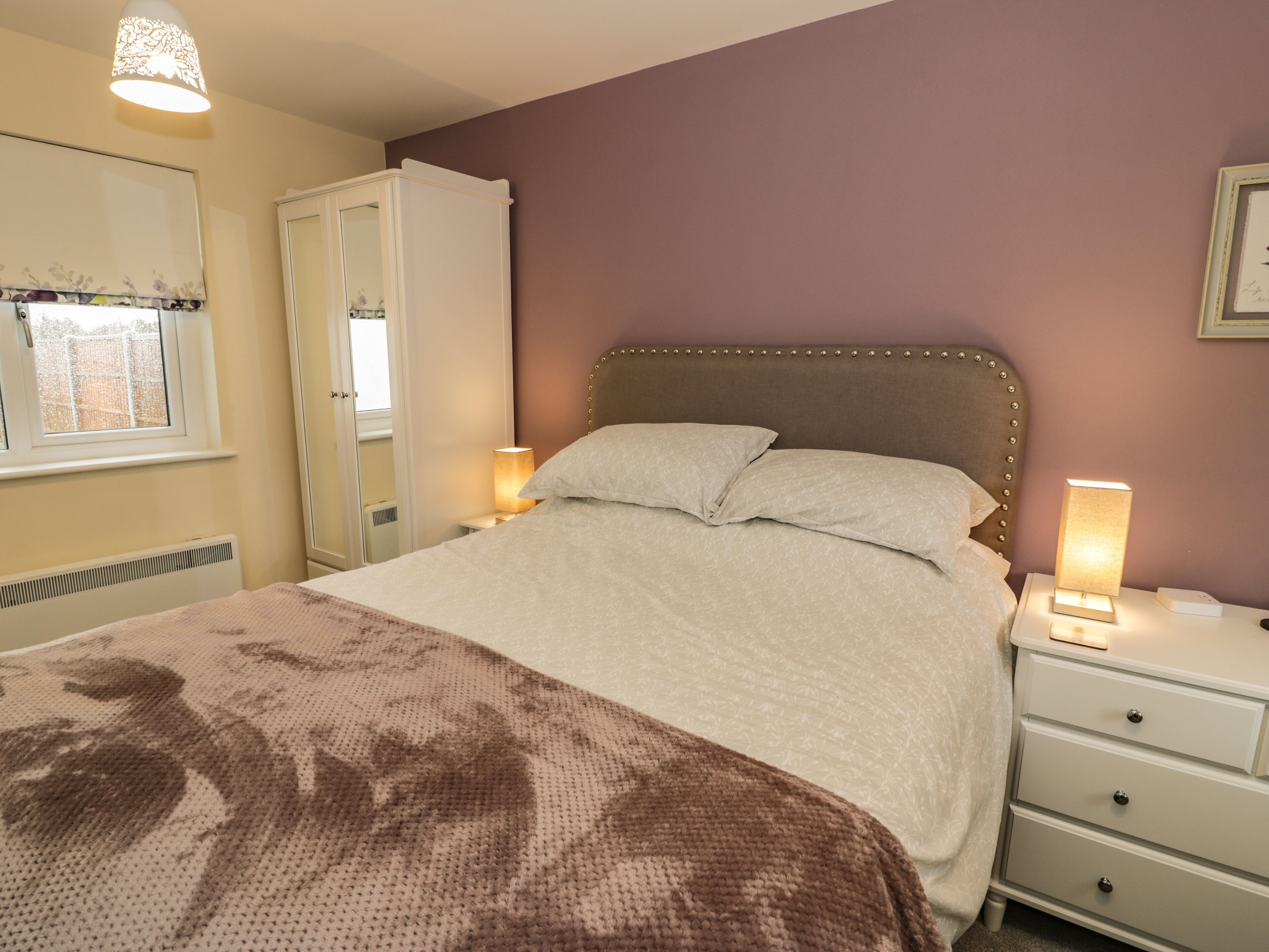 A bedroom with a bed, bedside lamps, a nightstand, and a window with a view.