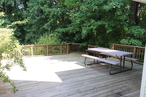 Een houten terras met een picknicktafel en bankjes, omringd door weelderige groene beplanting.