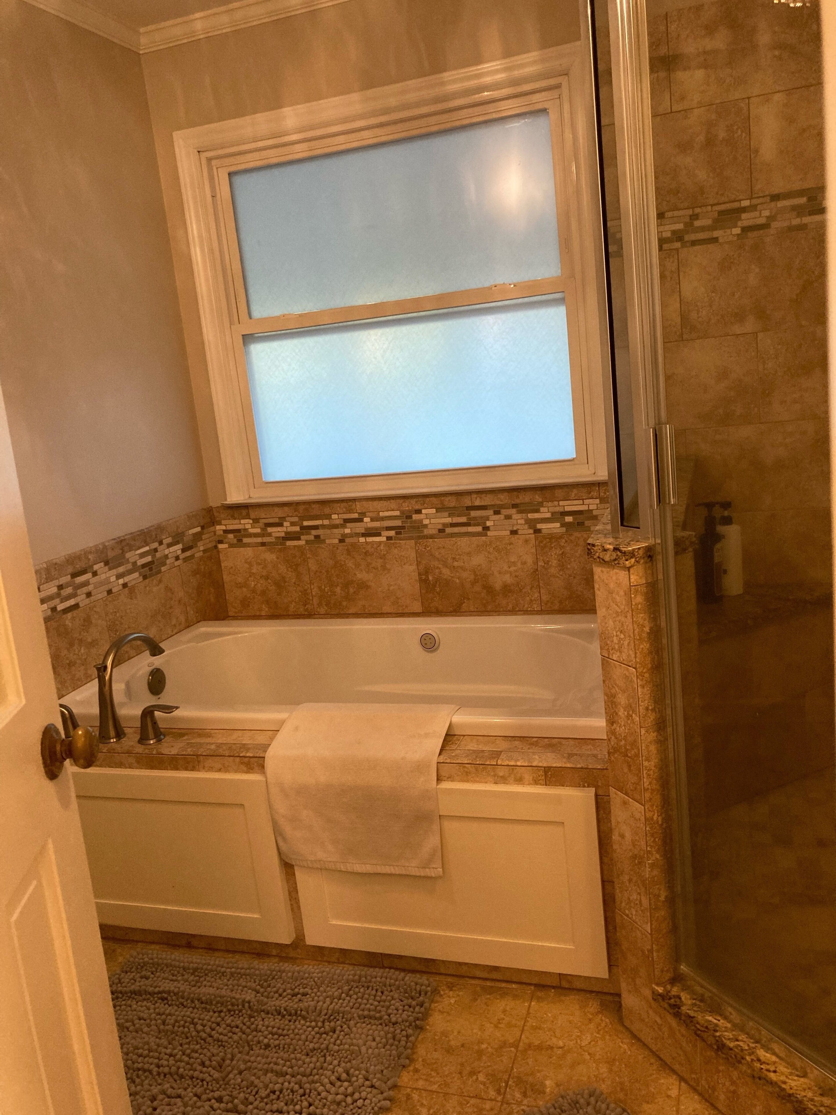 A bathroom with a bathtub, a glass-enclosed shower, and a window above the sink.