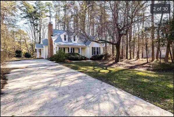 A two-story house with a front yard, a driveway, and a wooded area.