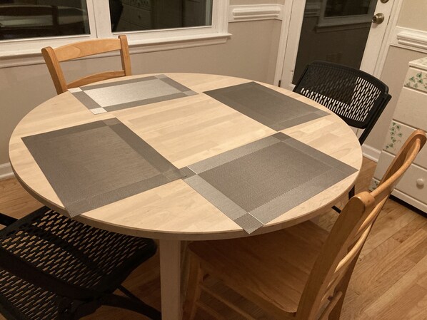 A round dining table with a checkered table runner and four chairs, one of which is black mesh.