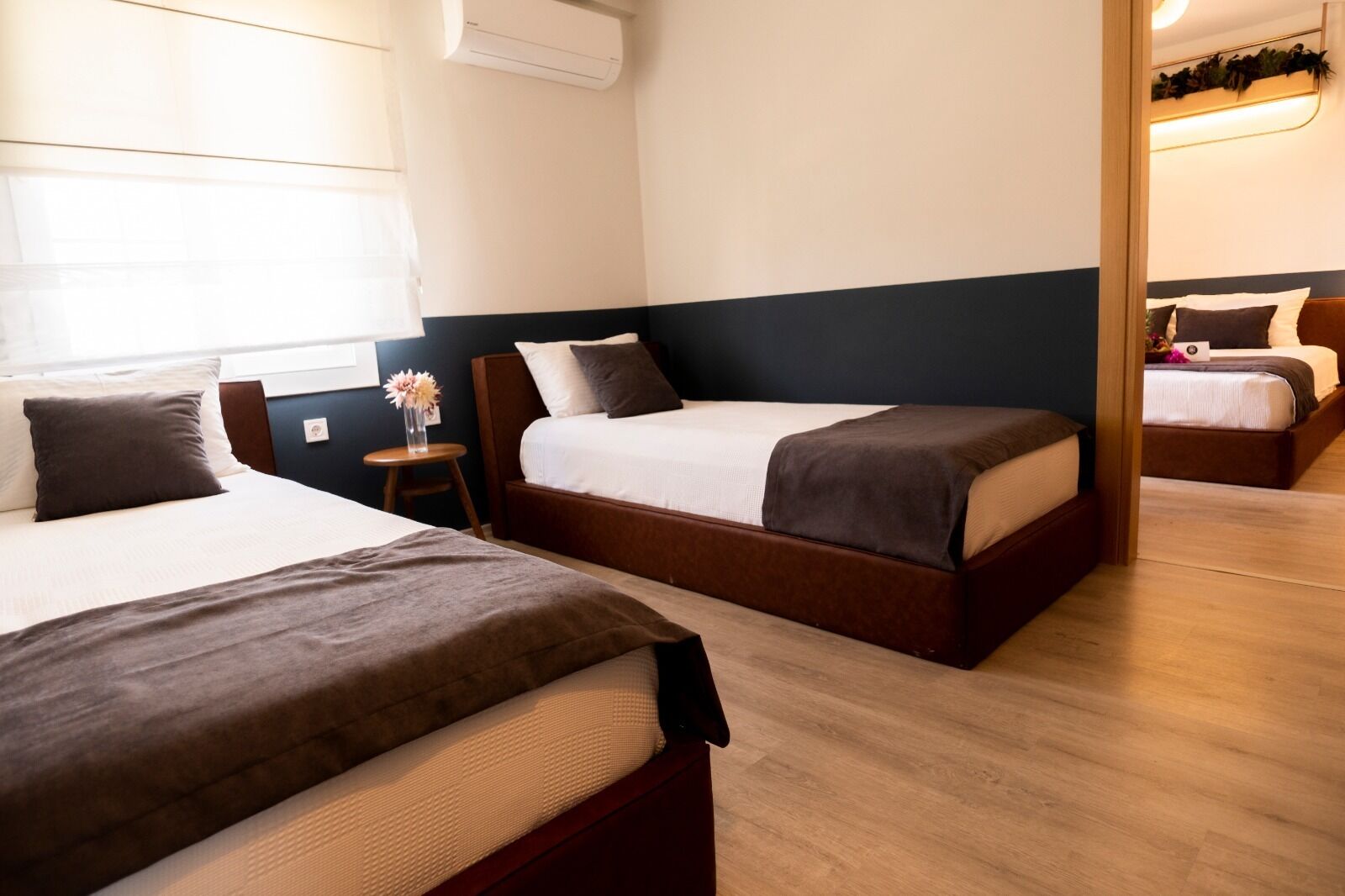Habitación de hotel con dos camas, una mesita con un florero y un espejo que refleja la habitación.