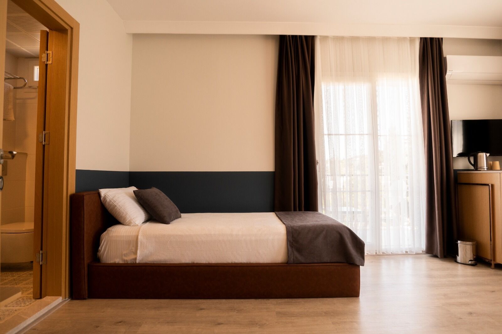 Una habitación de hotel con una cama, un armario de madera, un televisor y una ventana con cortinas.